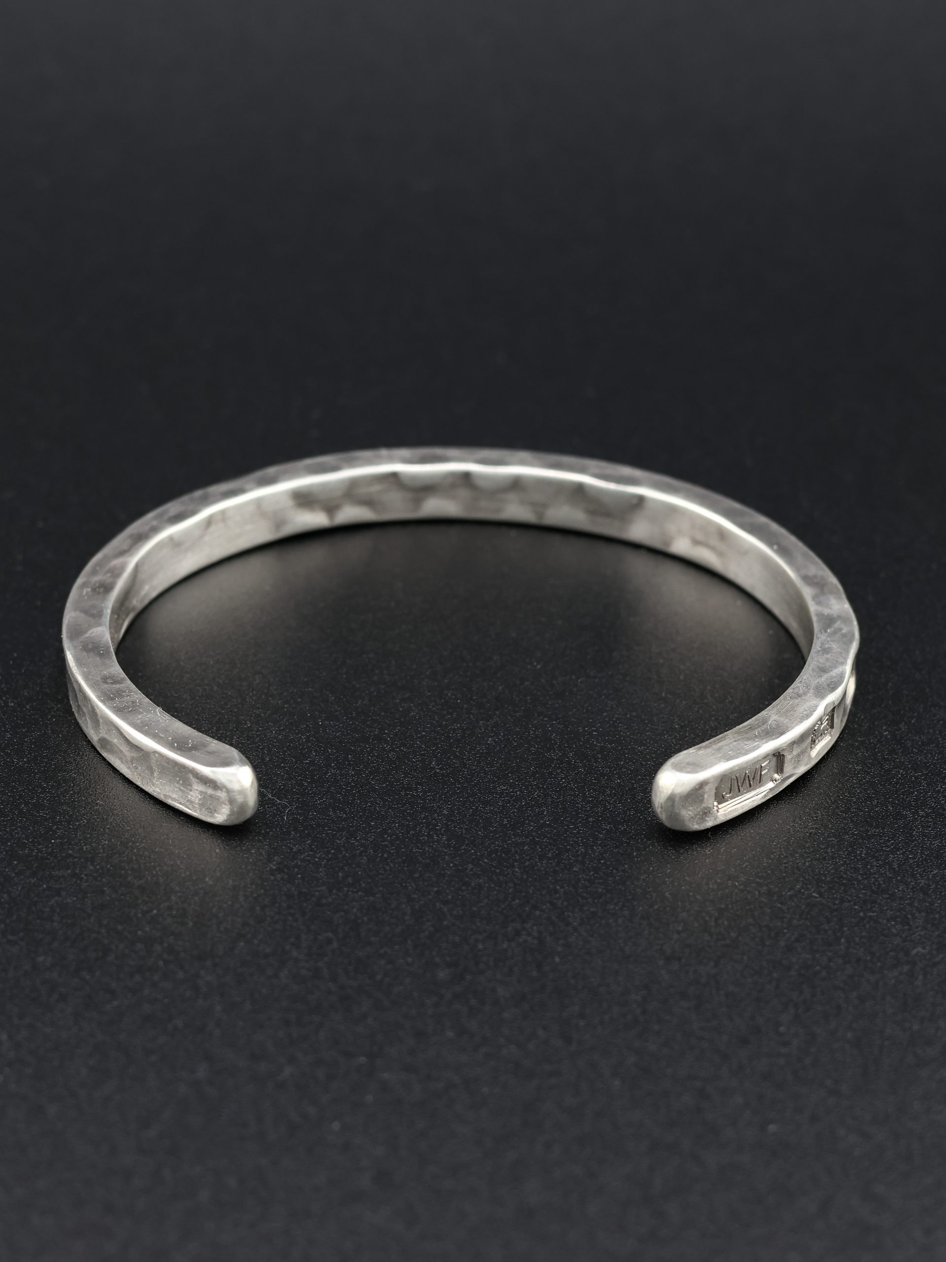 9E2A1918 Heavy sterling silver men's open cuff bracelet. It is finished in a hammered texture and incorporates large struck hallmarks on the outside of the cuff. It makes a perfect gift for men who value quality. Handmade in Devon, Newton Abbot by award winning goldsmith, James French at JWF Unique Designs