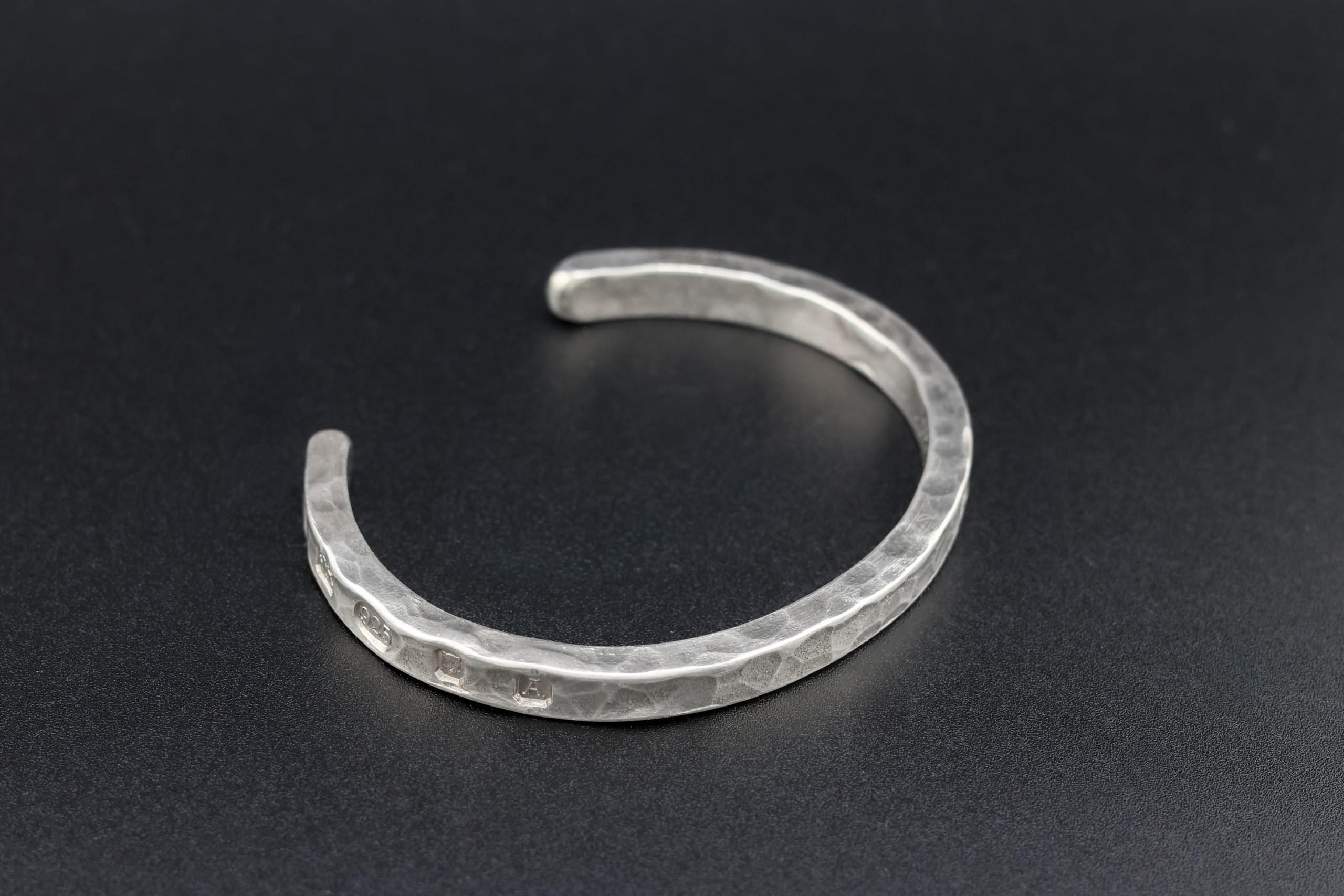 9E2A1922 Heavy sterling silver men's open cuff bracelet. It is finished in a hammered texture and incorporates large struck hallmarks on the outside of the cuff. It makes a perfect gift for men who value quality. Handmade in Devon, Newton Abbot by award winning goldsmith, James French at JWF Unique Designs