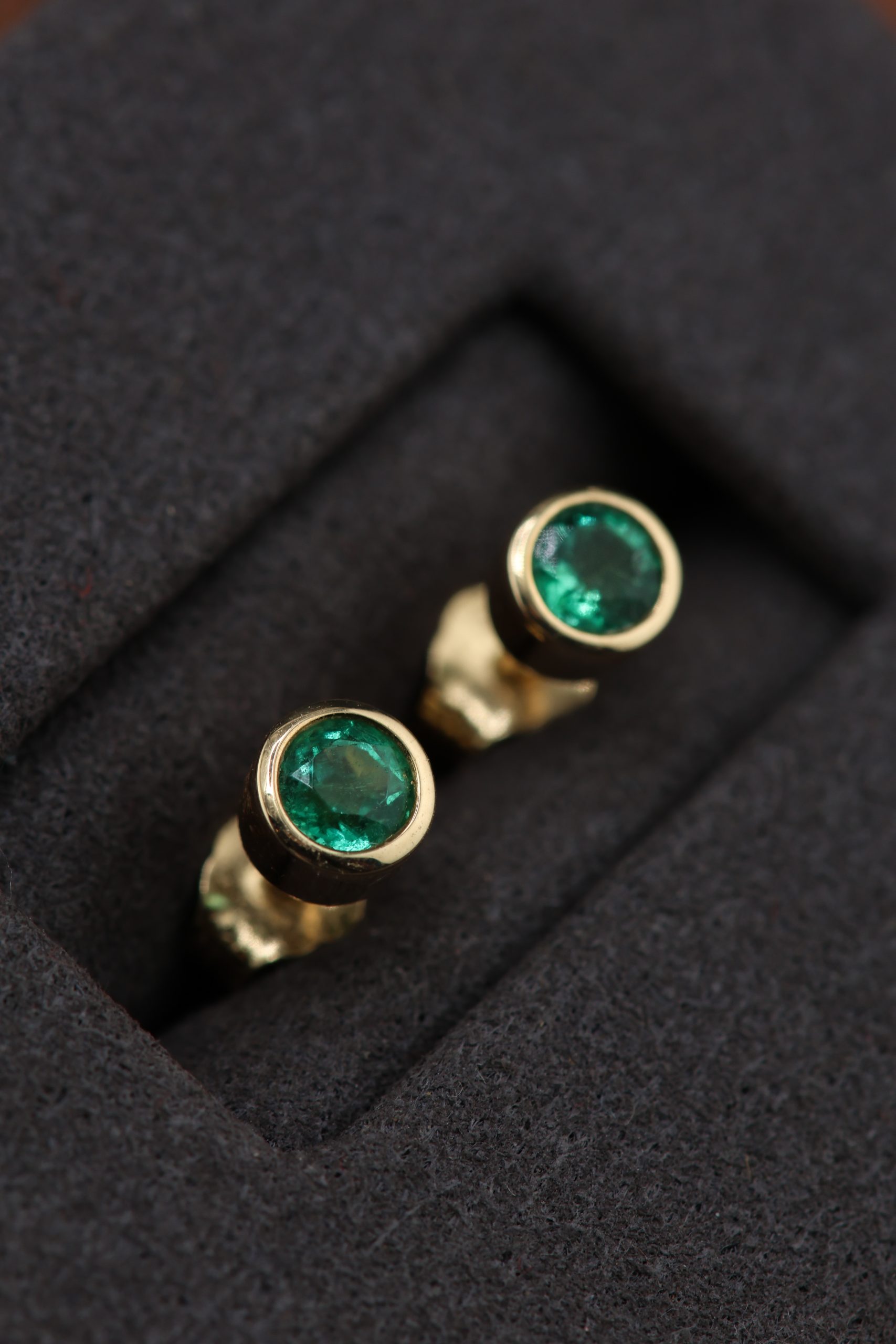 9E2A2319 Yellow gold emerald stud earrings. Designed and handcrafted by James French at JWF Unique Designs, in Devon, UK. The emerald stones are approximately 3.5mm in width and are in a bezel flush setting into 9ct and 18ct yellow gold. They are secured with yellow gold bitterly backs for security. These emerald stud earrings are timeless and classic and are an easy day wear. A brilliant gift for a loved one.