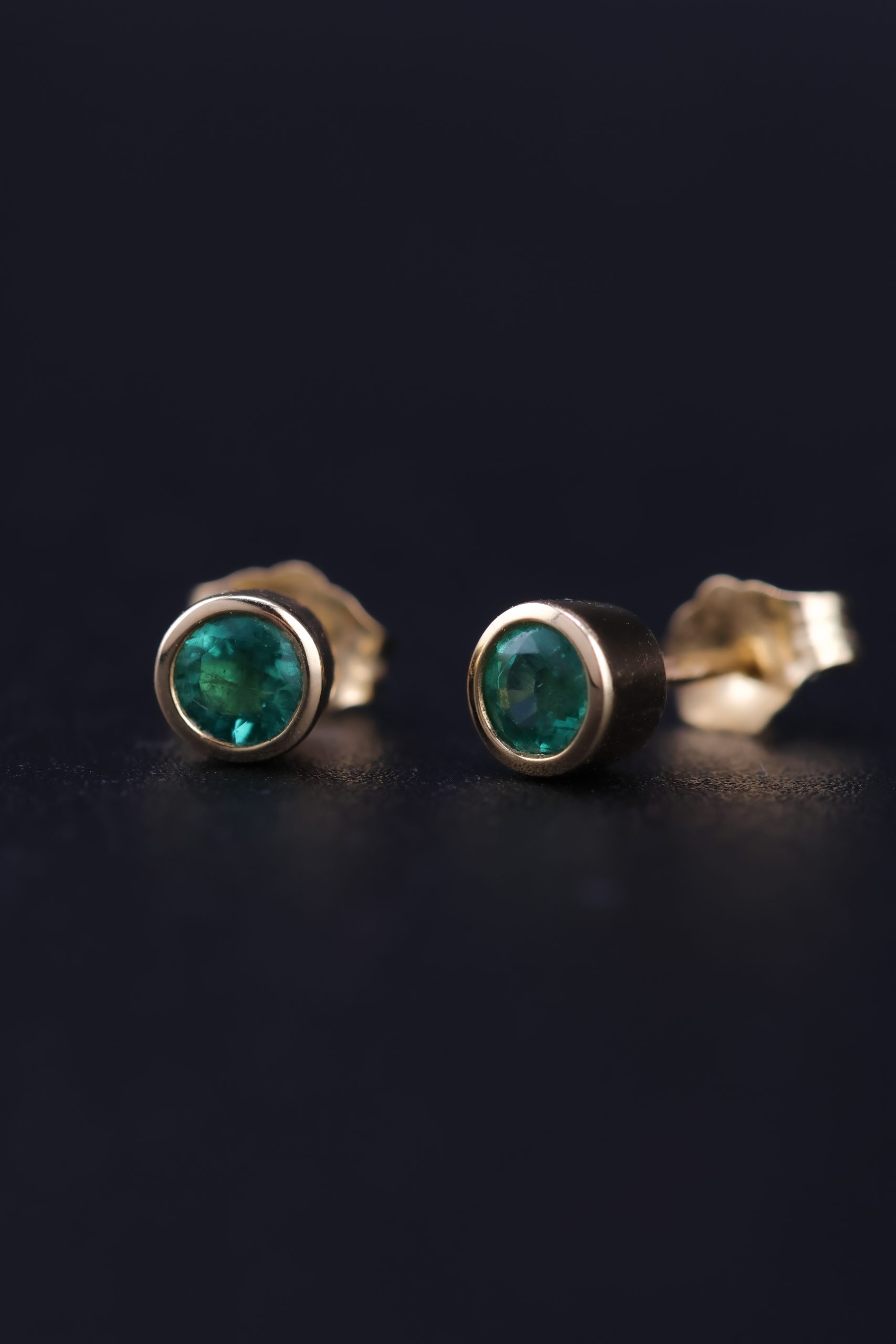 9E2A2354-2 Yellow gold emerald stud earrings. Designed and handcrafted by James French at JWF Unique Designs, in Devon, UK. The emerald stones are approximately 3.5mm in width and are in a bezel flush setting into 9ct and 18ct yellow gold. They are secured with yellow gold bitterly backs for security. These emerald stud earrings are timeless and classic and are an easy day wear. A brilliant gift for a loved one.