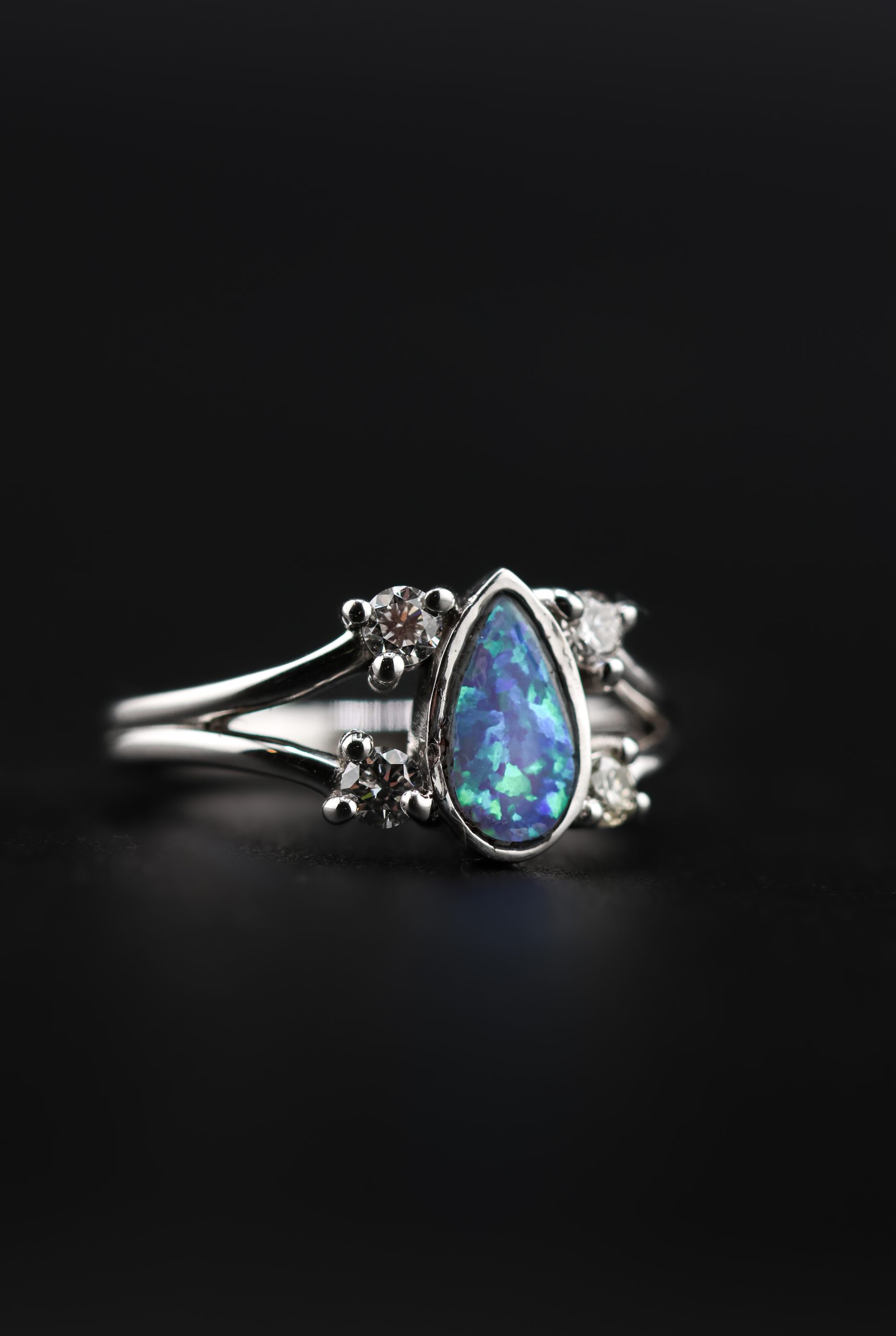 9E2A4368 White gold engagement ring with a pear-shaped opal centre stone. Four round diamonds set along a split shank design. Available in 9ct or 18ct white gold. Platinum plated for added brightness and protection. Handmade in Devon, UK by award-winning goldsmith James French.