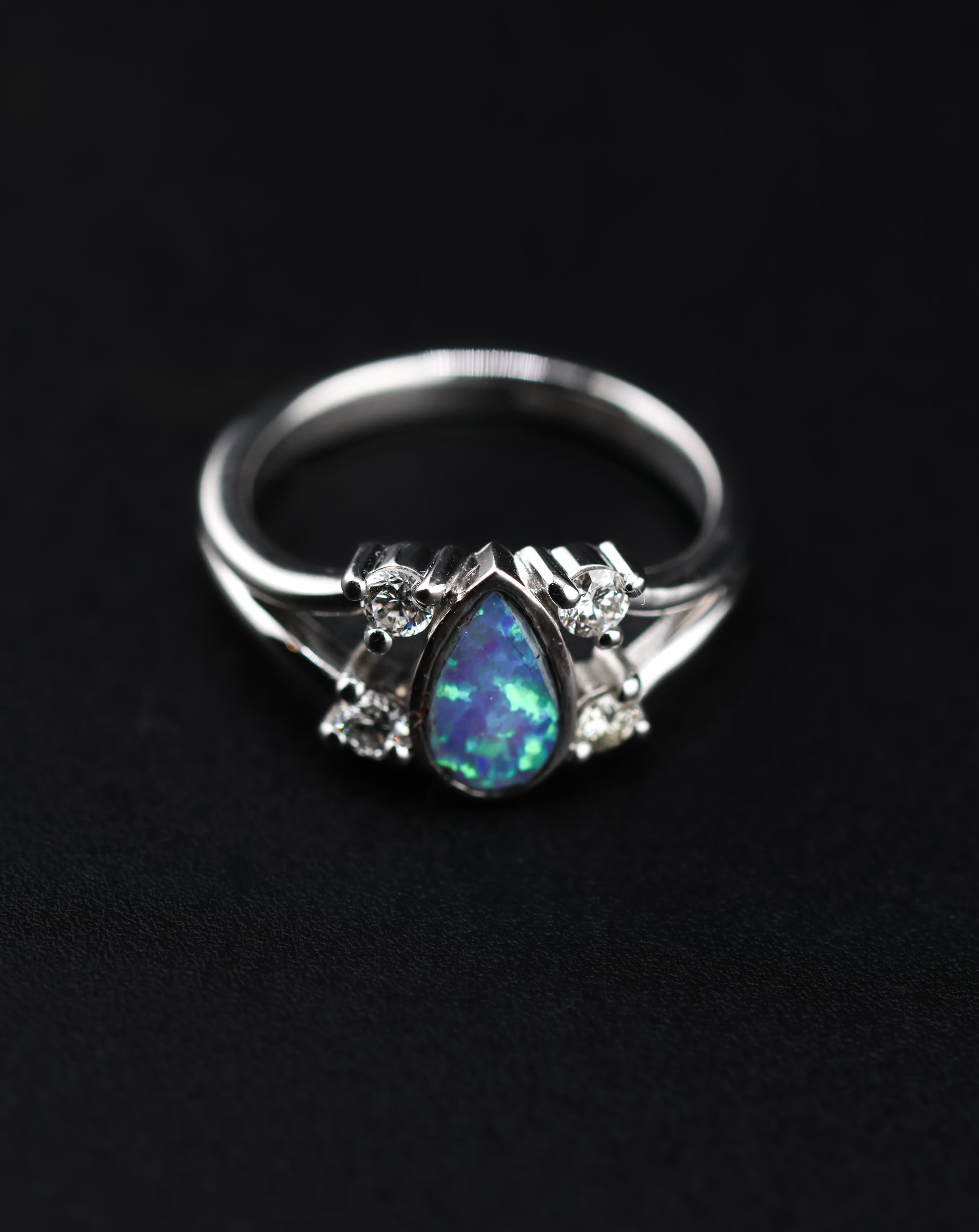 9E2A4373 White gold engagement ring with a pear-shaped opal centre stone. Four round diamonds set along a split shank design. Available in 9ct or 18ct white gold. Platinum plated for added brightness and protection. Handmade in Devon, UK by award-winning goldsmith James French.