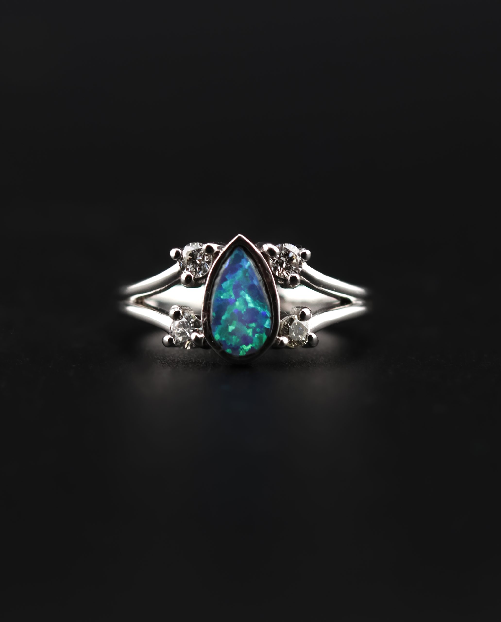 9E2A4375 White gold engagement ring with a pear-shaped opal centre stone. Four round diamonds set along a split shank design. Available in 9ct or 18ct white gold. Platinum plated for added brightness and protection. Handmade in Devon, UK by award-winning goldsmith James French.