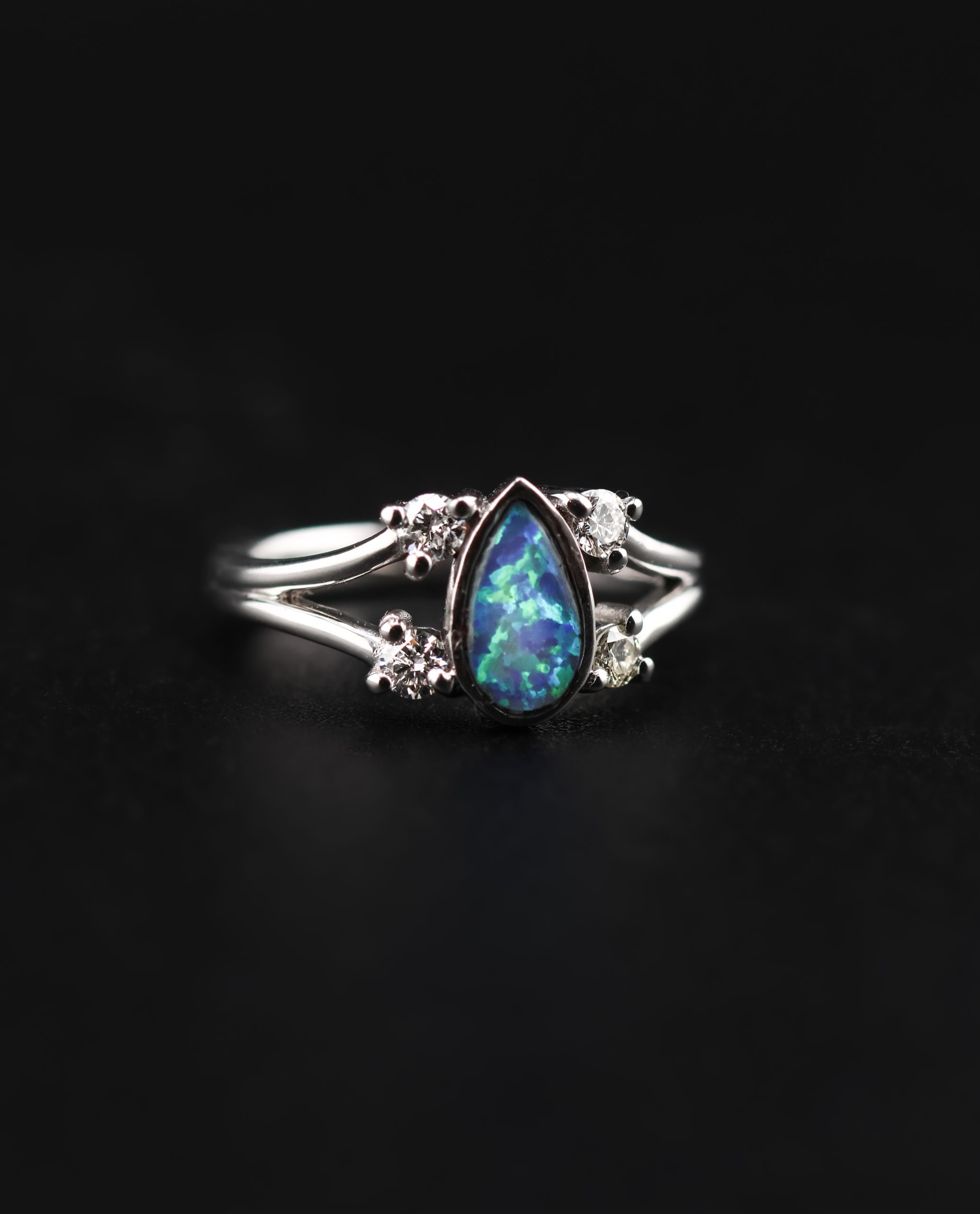 9E2A4376 White gold engagement ring with a pear-shaped opal centre stone. Four round diamonds set along a split shank design. Available in 9ct or 18ct white gold. Platinum plated for added brightness and protection. Handmade in Devon, UK by award-winning goldsmith James French.