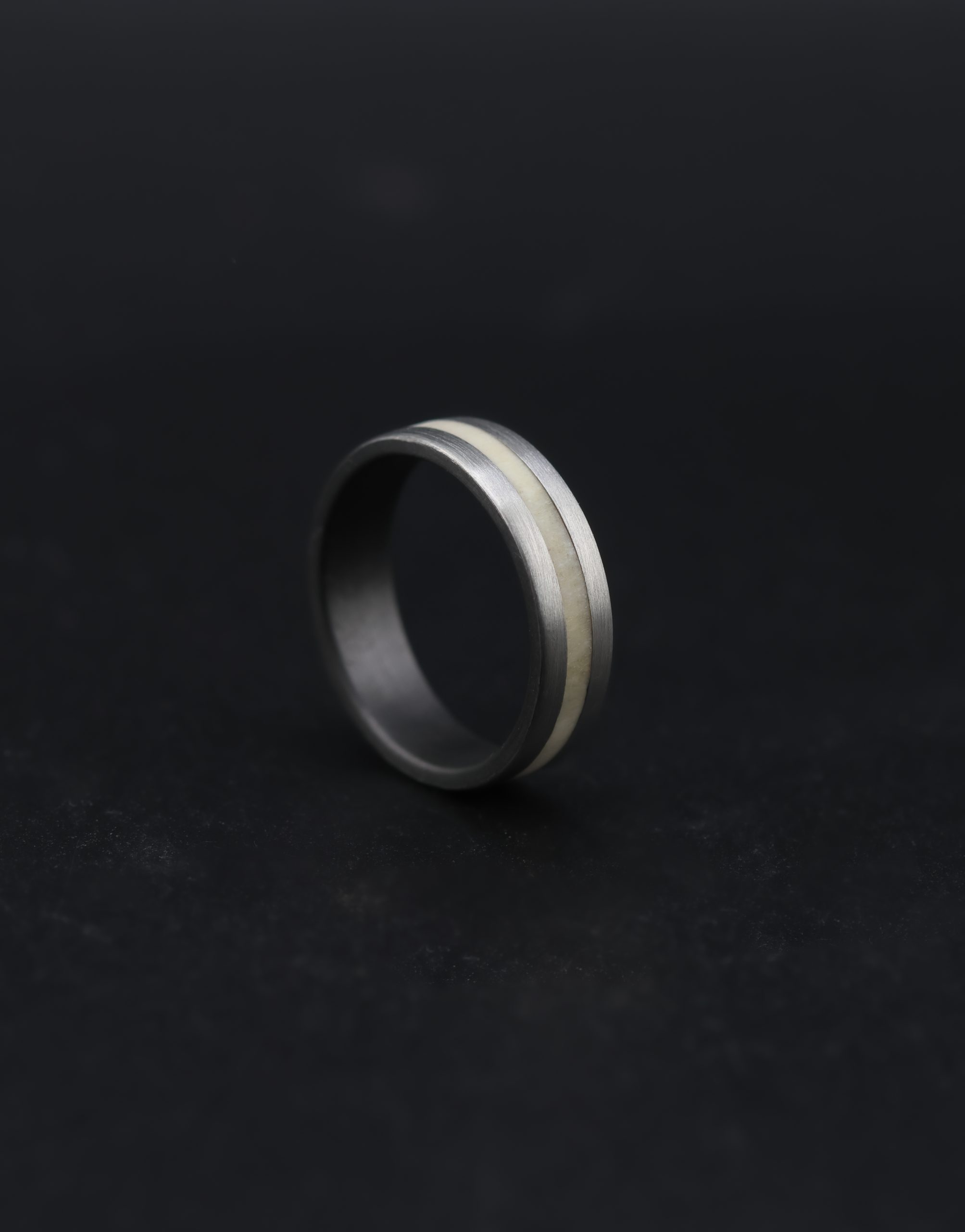 9E2A4457-2 Natural silver-grey zirconium wedding ring with a central deer antler inlay. 6mm wide flat profile with slightly rounded corners. Smooth satin finish. Lightweight and durable men's wedding ring. Handmade in Devon, UK by James French.