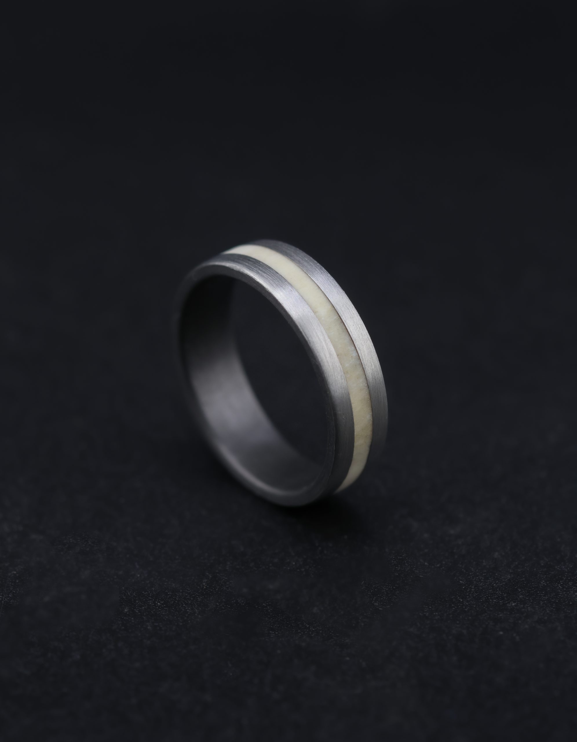 9E2A4459 Natural silver-grey zirconium wedding ring with a central deer antler inlay. 6mm wide flat profile with slightly rounded corners. Smooth satin finish. Lightweight and durable men's wedding ring. Handmade in Devon, UK by James French.