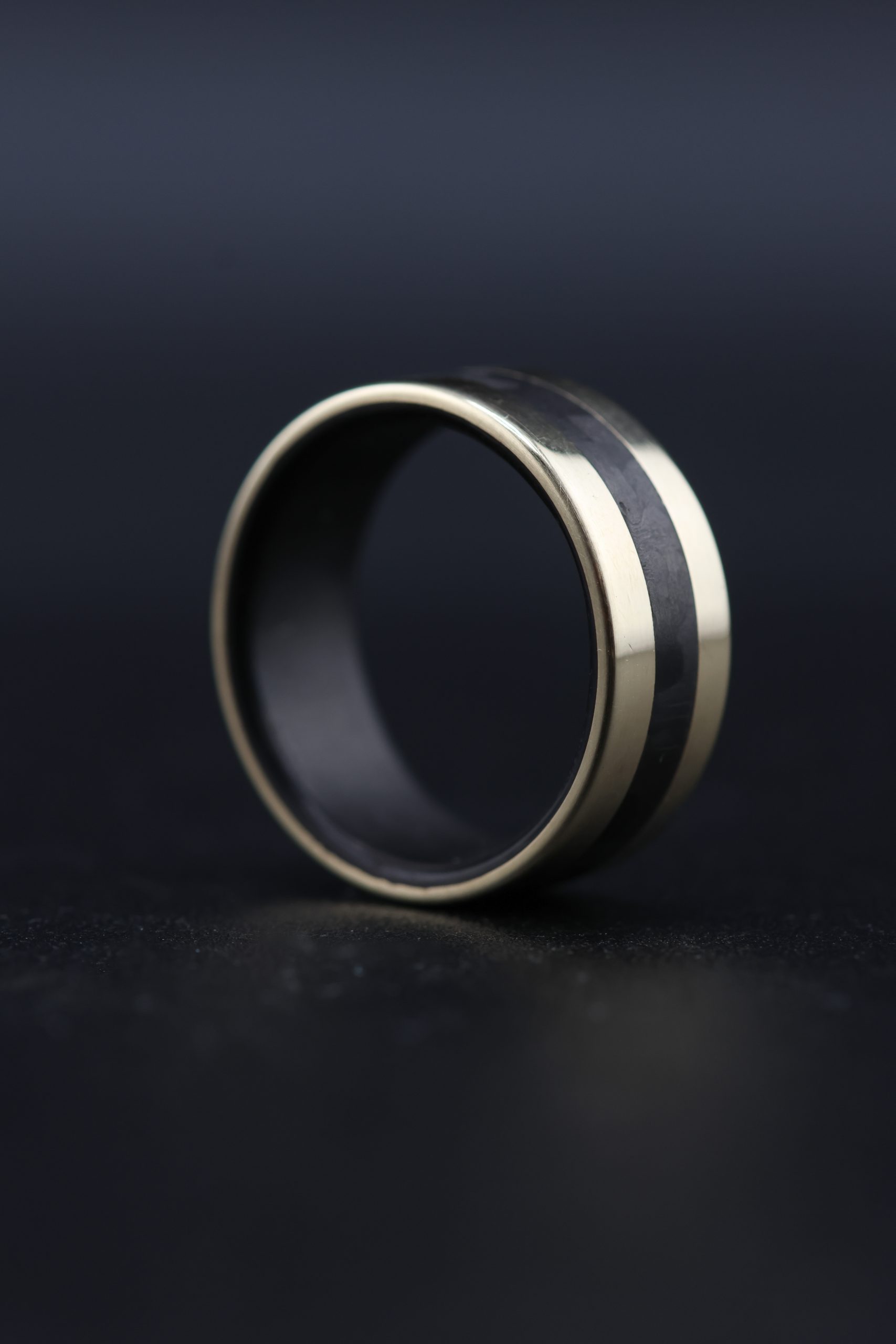 JWF 9ct yellow gold wedding ring with black carbon fibre inlay and liner. Flat profile band with polished finish. 3mm carbon fibre centre inlay. 9mm wide men's wedding ring. Handmade in Devon, UK by award-winning goldsmith James French.