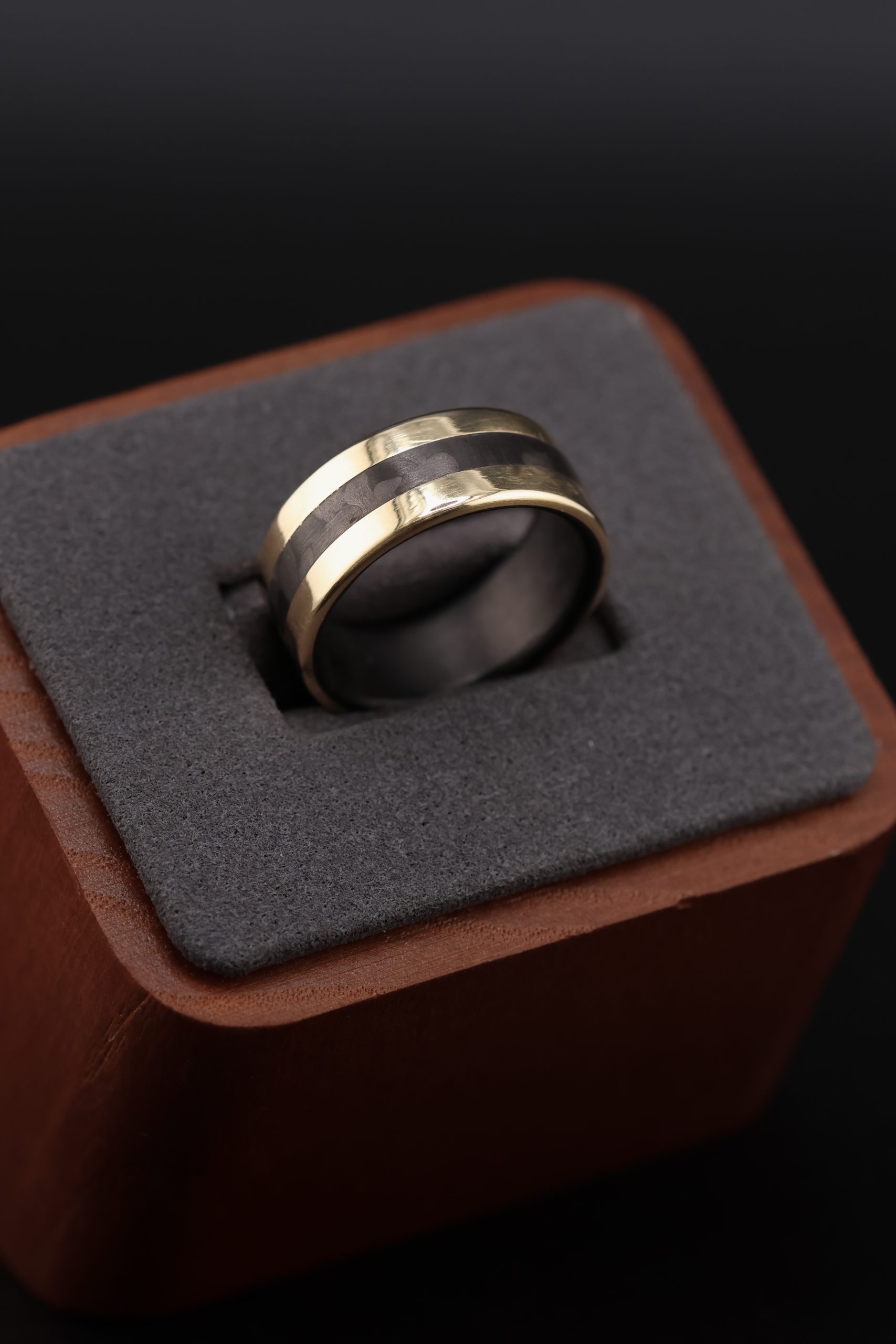 9E2A5690 9ct yellow gold wedding ring with black carbon fibre inlay and liner. Flat profile band with polished finish. 3mm carbon fibre centre inlay. 9mm wide men's wedding ring. Handmade in Devon, UK by award-winning goldsmith James French.