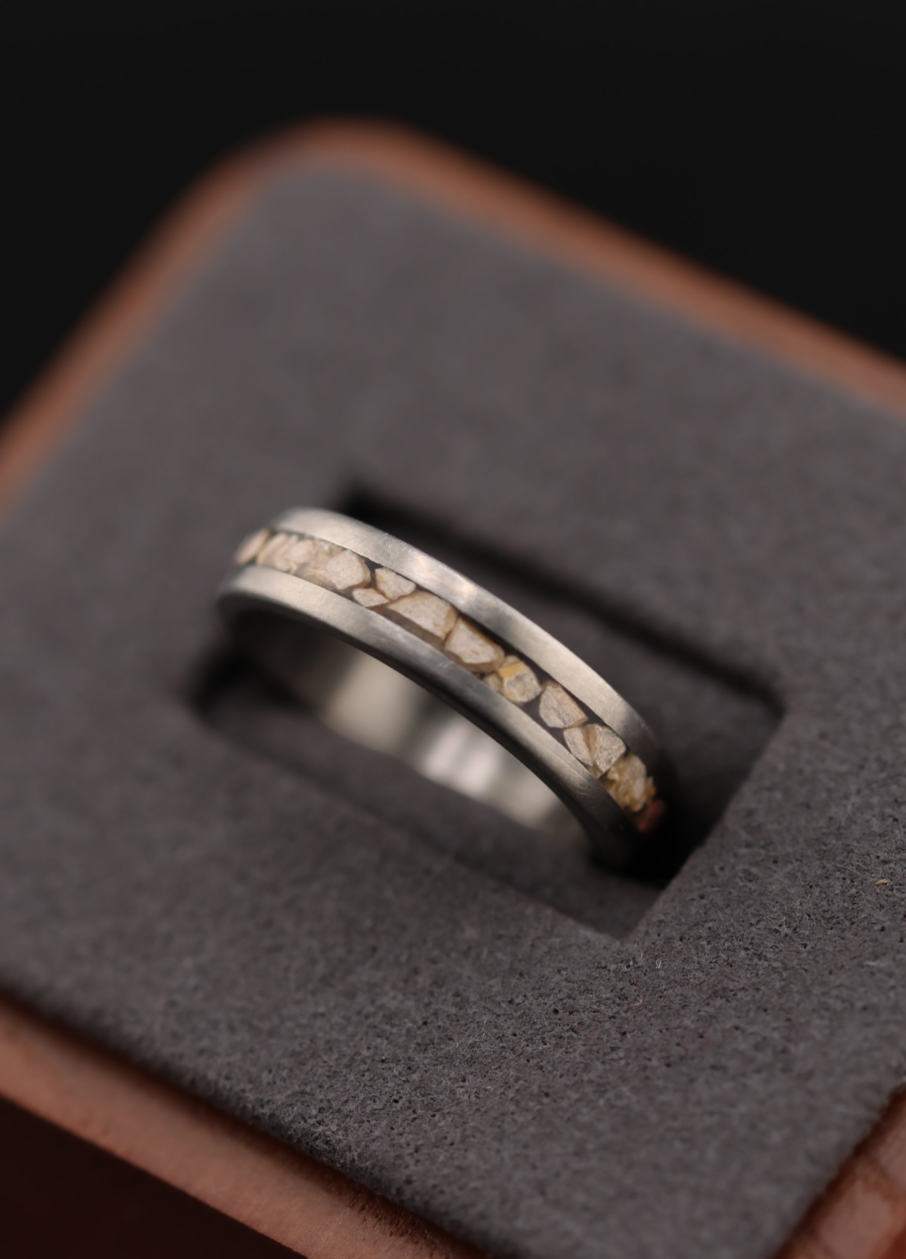 9E2A3875 Titanium dinosaur fossil wedding ring. 5mm wide band featuring certified fossilised Stegosaurus dinosaur bone and Lightweight and durable men's wedding ring. Handmade in Devon, UK by award-winning goldsmith James Frenc