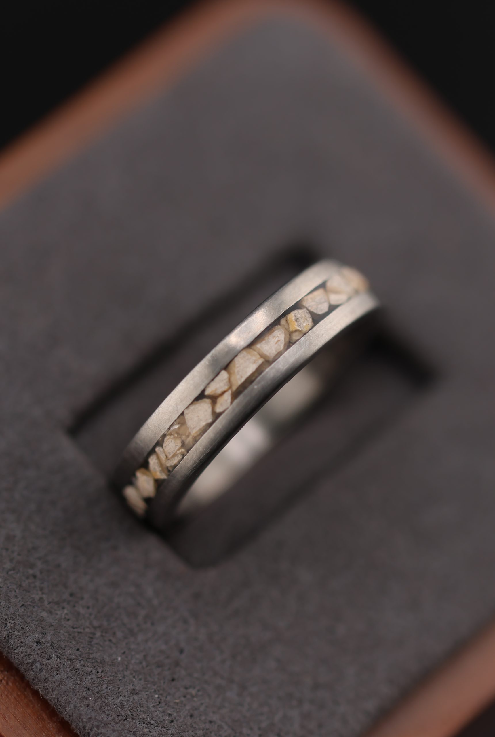 9E2A3877 Titanium dinosaur fossil wedding ring. 5mm wide band featuring certified fossilised Stegosaurus dinosaur bone and Lightweight and durable men's wedding ring. Handmade in Devon, UK by award-winning goldsmith James Frenc