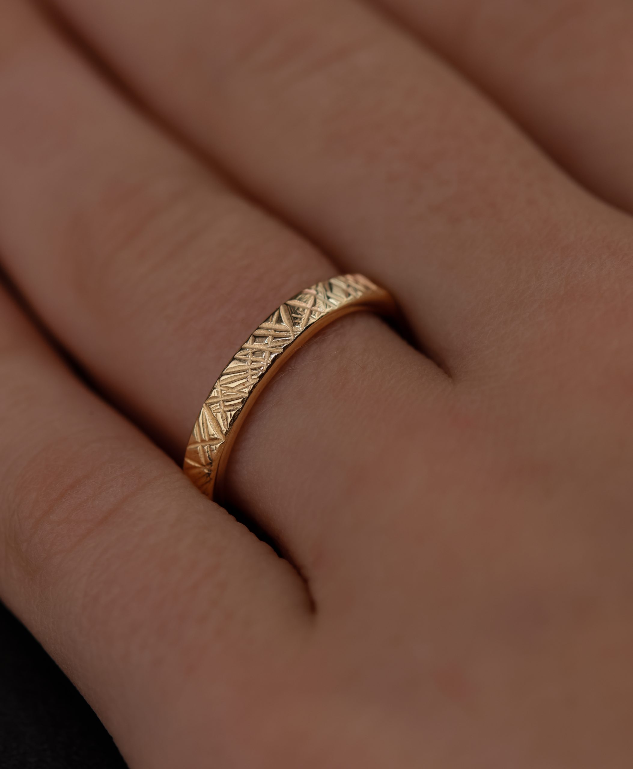 9E2A5765 A slim 2.5mm wedding ring made from polished 9ct yellow gold. The flat profile features an angular Prism hammered texture that catches and reflects the light. This textured yellow gold wedding ring is handmade in Devon by goldsmith James French.