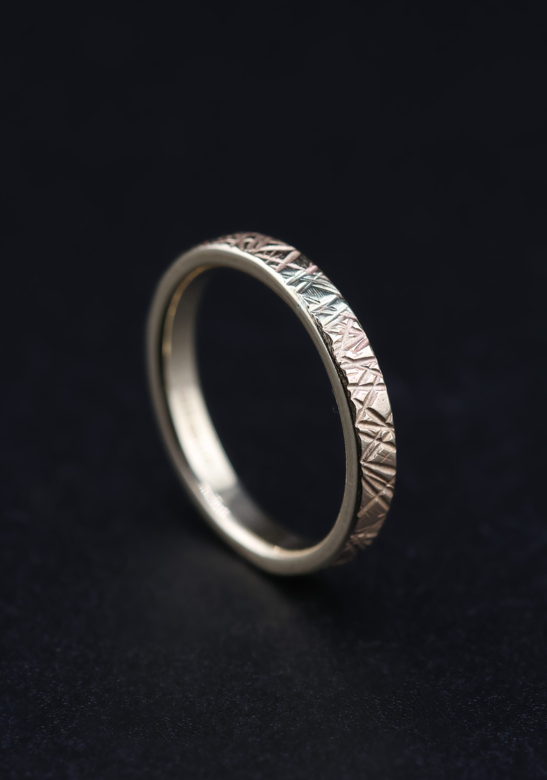 9E2A5769 A slim 2.5mm wedding ring made from polished 9ct yellow gold. The flat profile features an angular Prism hammered texture that catches and reflects the light. This textured yellow gold wedding ring is handmade in Devon by goldsmith James French.
