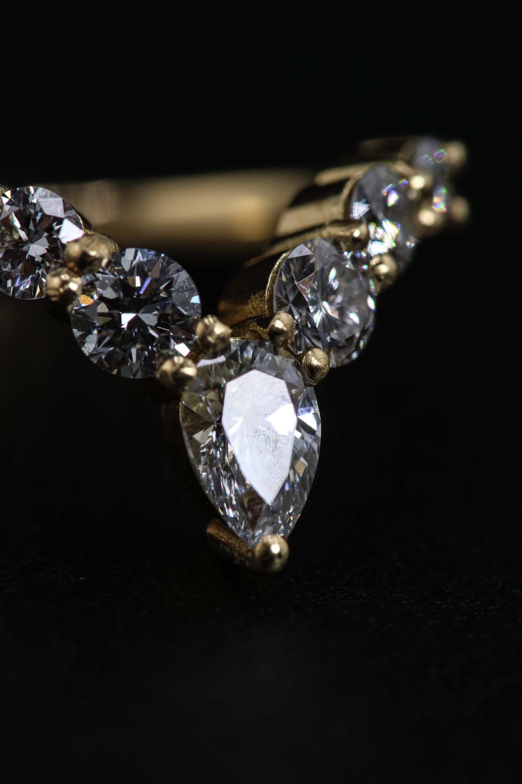 9E2A5819 An 18ct yellow gold shaped wedding ring designed to fit around an engagement ring. The swept design features a central pear-shaped diamond with round natural and lab-grown diamonds flowing along the curved shank. This bespoke diamond wedding ring has a high-polished finish. Handmade in Devon by goldsmith James French.