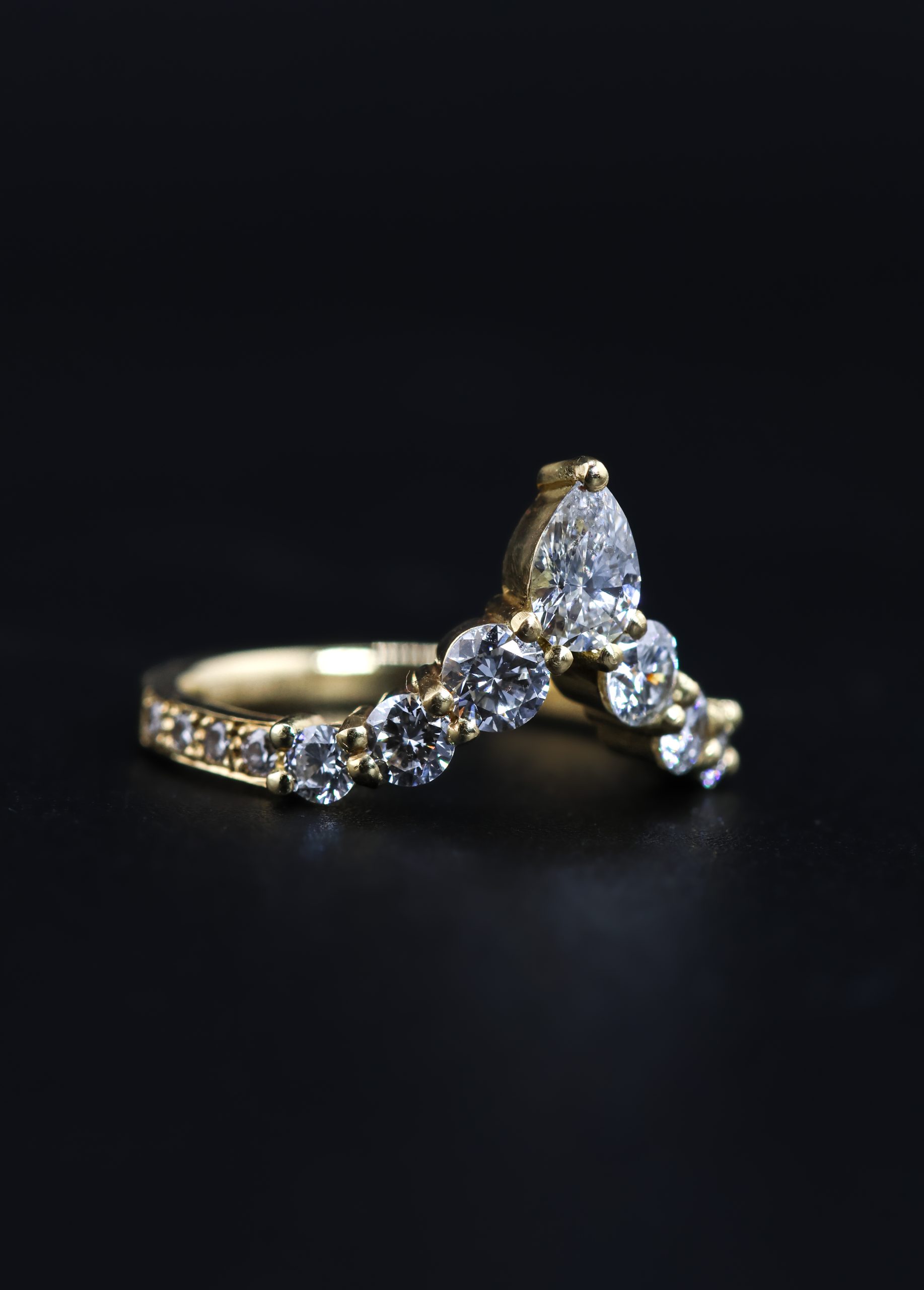 9E2A5826 An 18ct yellow gold shaped wedding ring designed to fit around an engagement ring. The swept design features a central pear-shaped diamond with round natural and lab-grown diamonds flowing along the curved shank. This bespoke diamond wedding ring has a high-polished finish. Handmade in Devon by goldsmith James French.