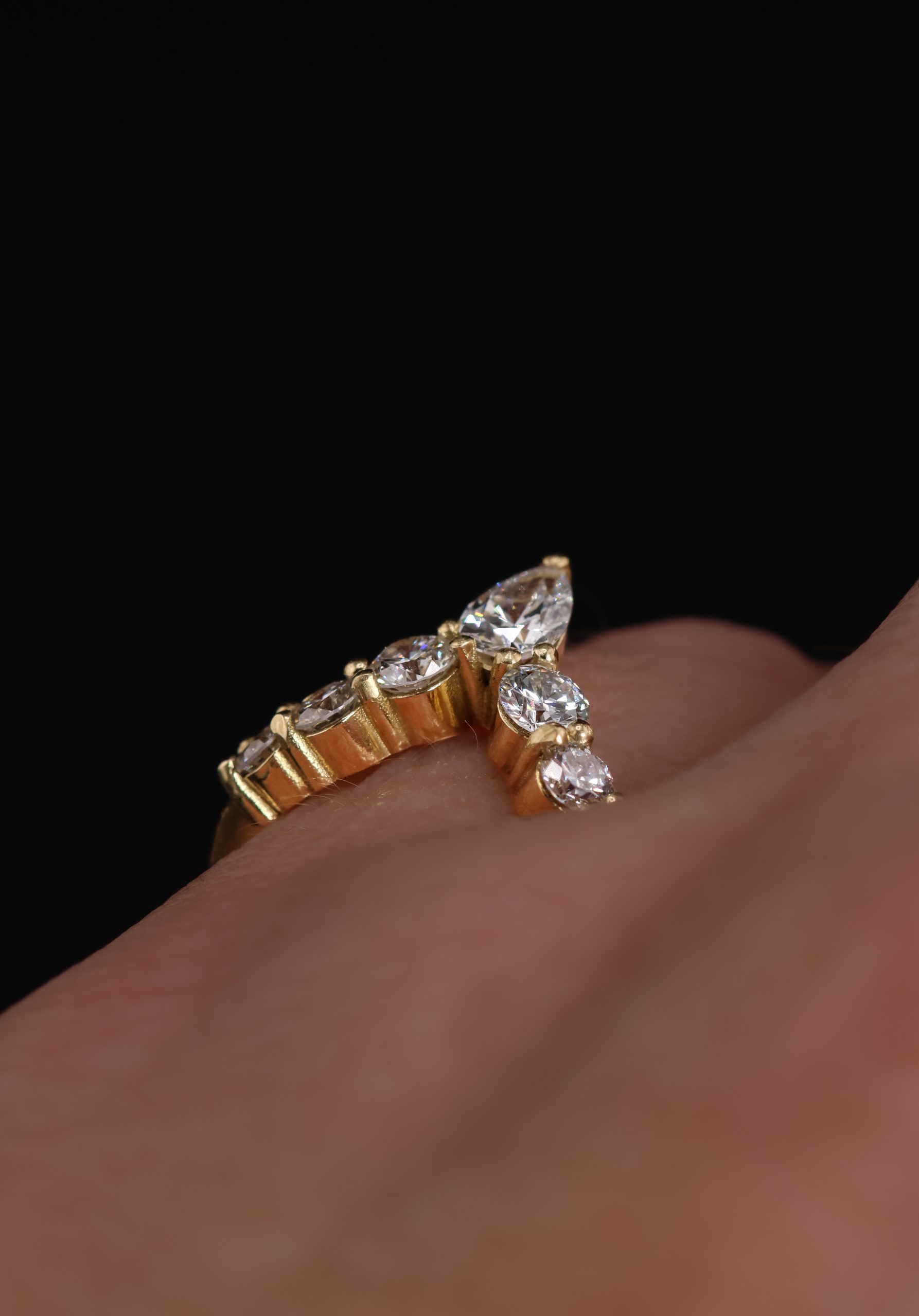 9E2A5834 An 18ct yellow gold shaped wedding ring designed to fit around an engagement ring. The swept design features a central pear-shaped diamond with round natural and lab-grown diamonds flowing along the curved shank. This bespoke diamond wedding ring has a high-polished finish. Handmade in Devon by goldsmith James French.