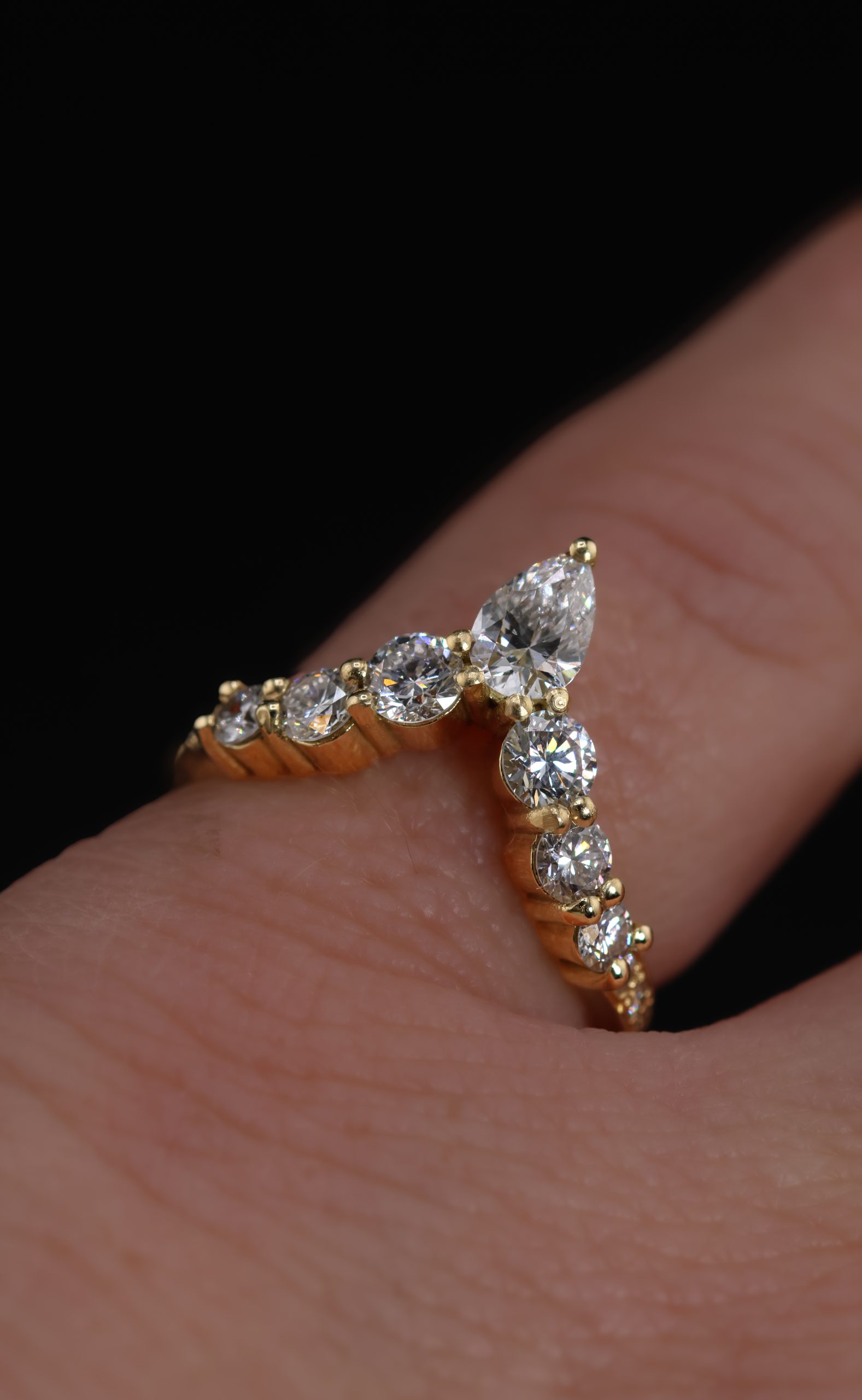 9E2A5836 An 18ct yellow gold shaped wedding ring designed to fit around an engagement ring. The swept design features a central pear-shaped diamond with round natural and lab-grown diamonds flowing along the curved shank. This bespoke diamond wedding ring has a high-polished finish. Handmade in Devon by goldsmith James French.