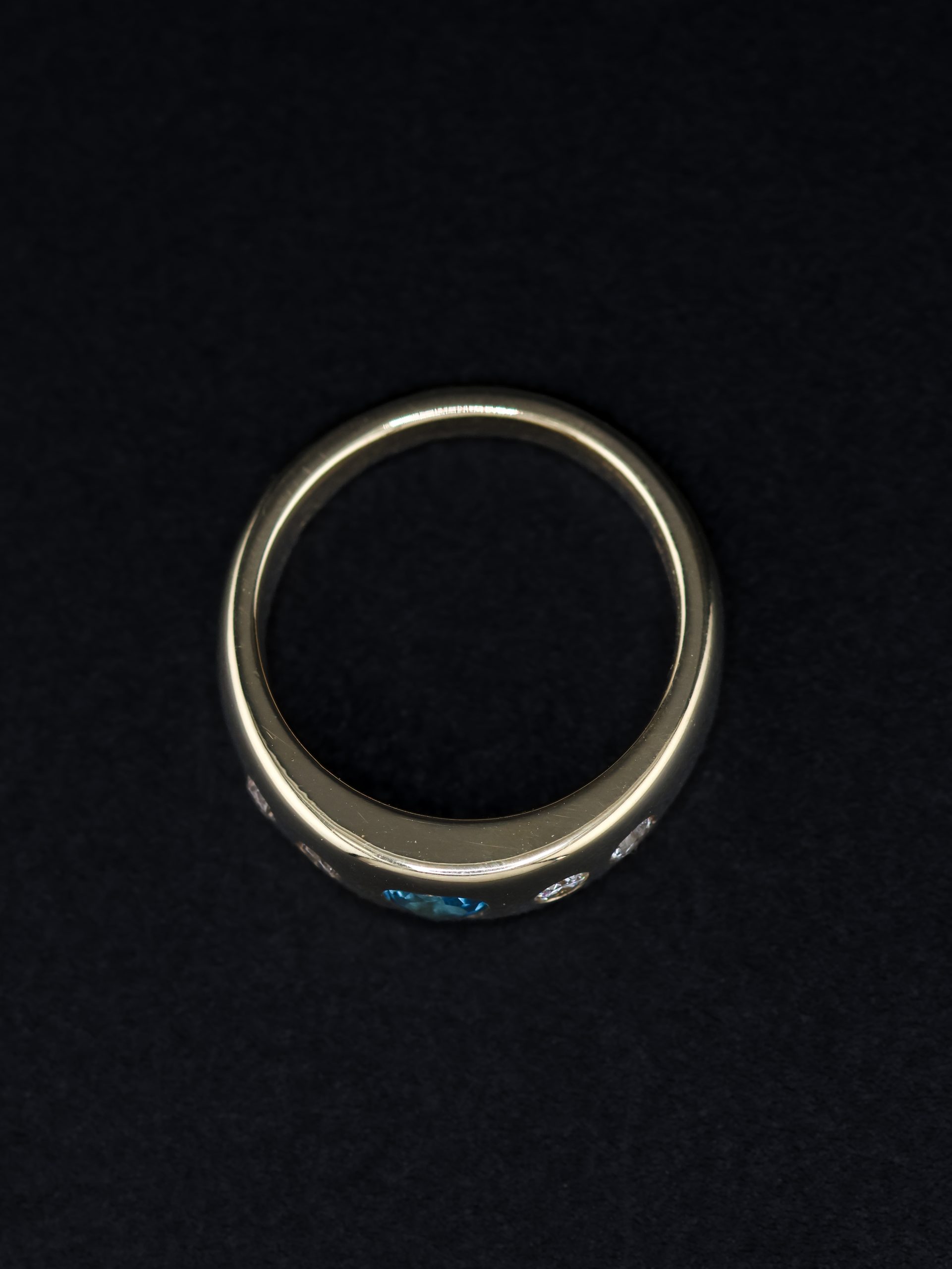 9E2A5866 A wide yellow gold ring featuring a heart-shaped blue topaz with two round diamonds on each side. The polished ring is handmade in Devon by goldsmith and silversmith James French.
