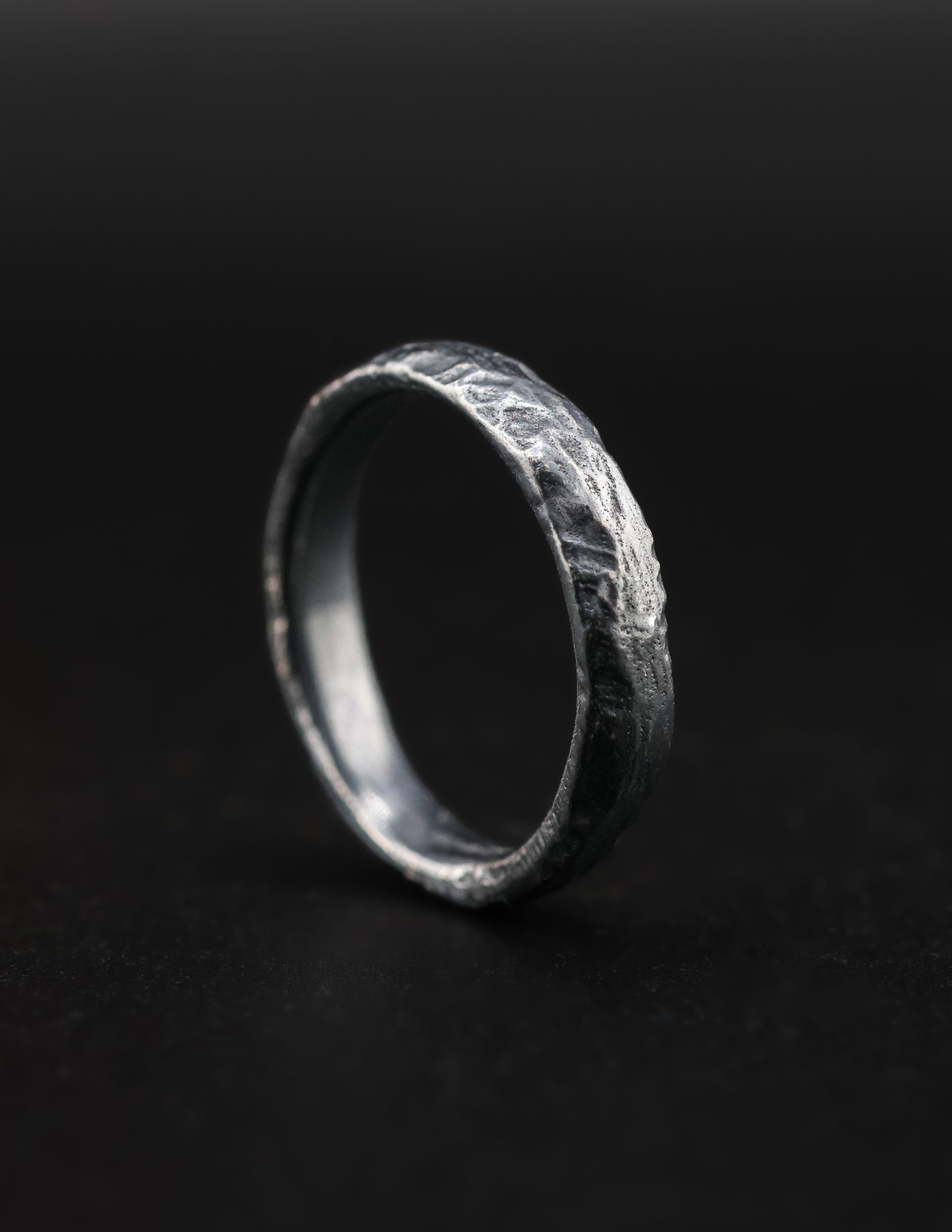 9E2A6416 A men’s sterling silver wedding ring with a dark riven texture and D-shape profile. The sand cast ring is handmade in Devon by goldsmith and silversmith James French.
