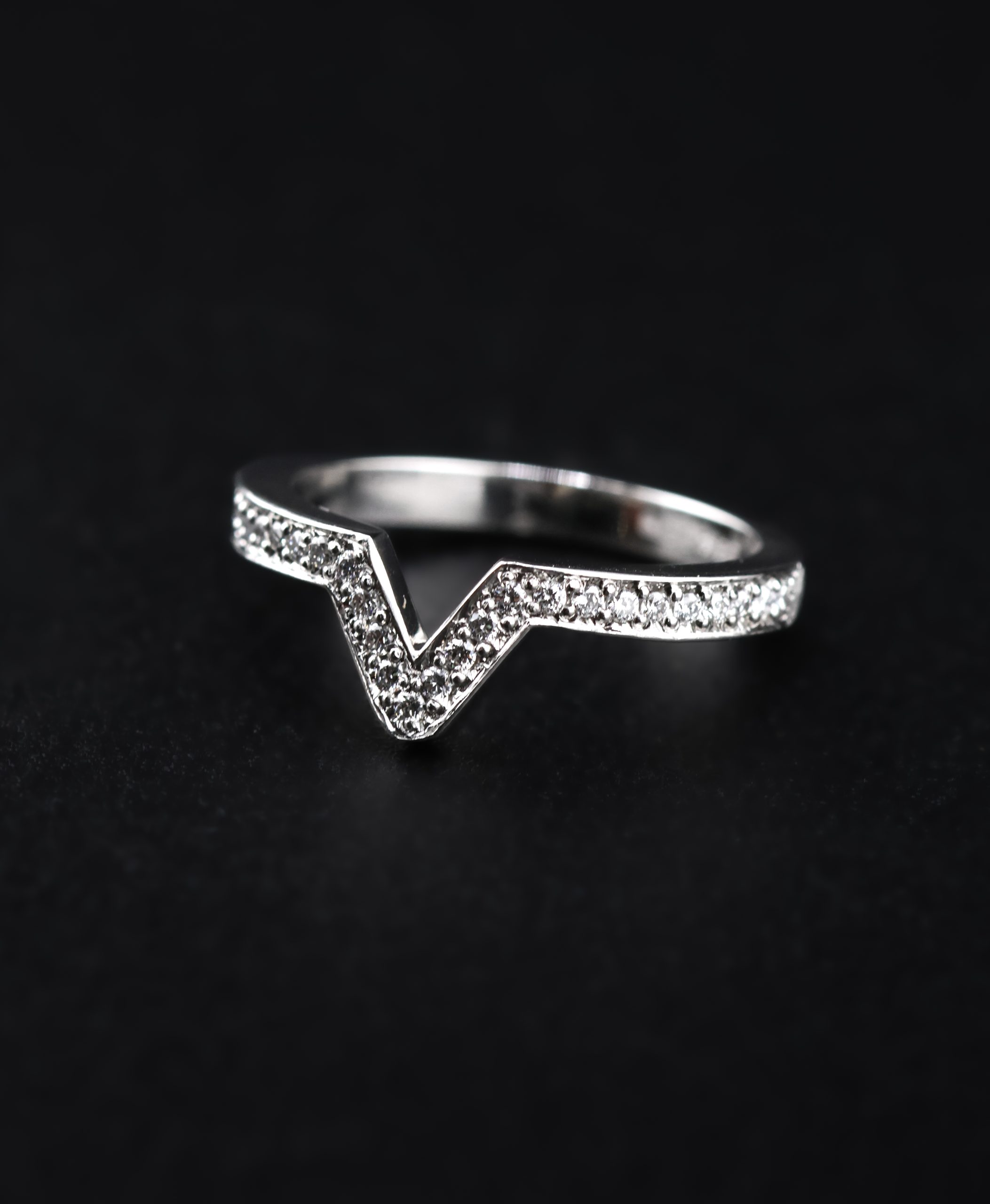 9E2A6435 A platinum diamond chevron wedding ring with micro-grain set natural diamonds and a defined V-shaped centre. The 2.5mm ring is designed to fit around an engagement ring. It is handmade in Devon by goldsmith and silversmith James French.