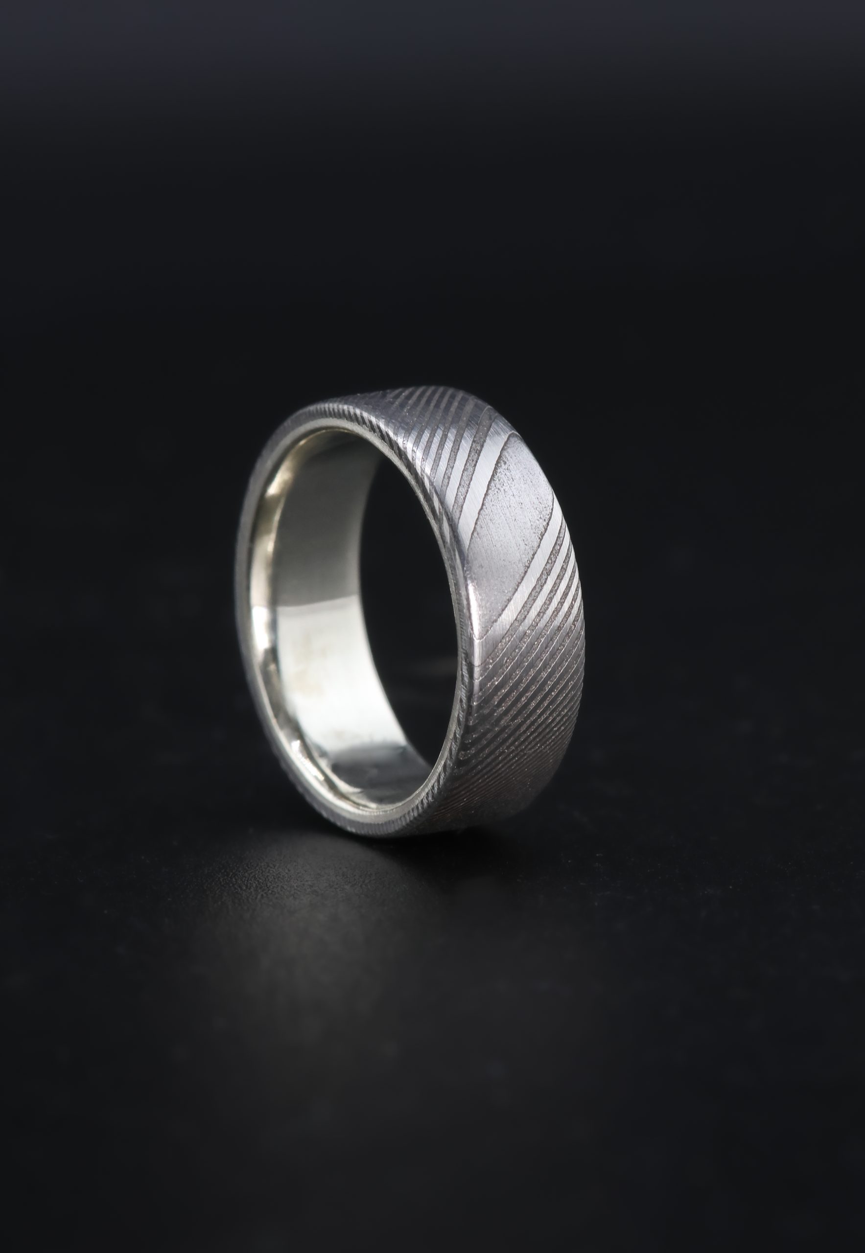 9E2A6464 A men’s twisted stainless steel Damascus wedding ring with a flat profile and platinum inner liner. It is handmade in Devon by goldsmith and silversmith James French.