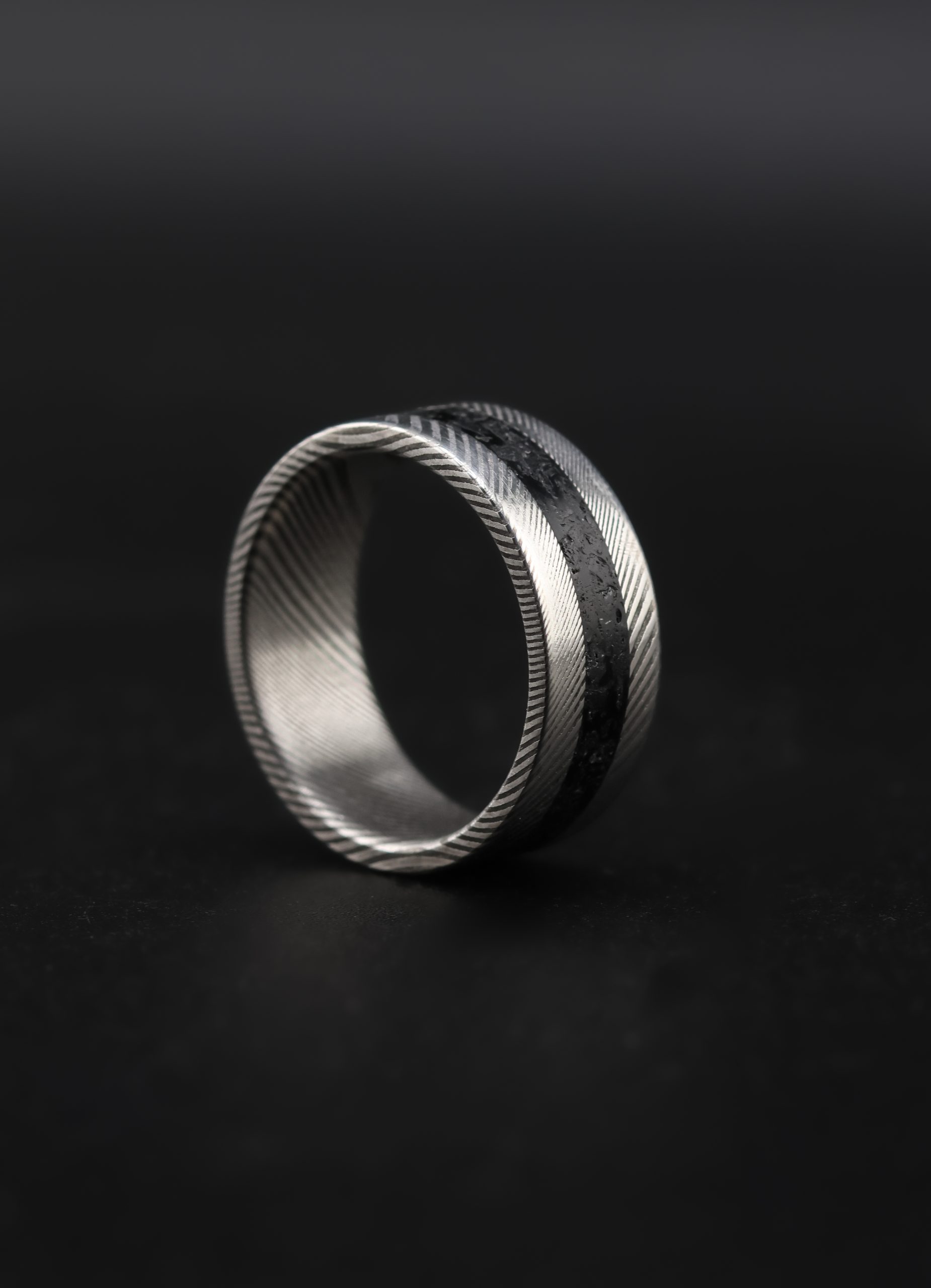 9E2A6537 An 8mm men’s wedding ring made from twisted stainless steel Damascus with a central black obsidian inlay. The ring has a flat profile and a lightweight, durable design. Handmade in Devon by James French.