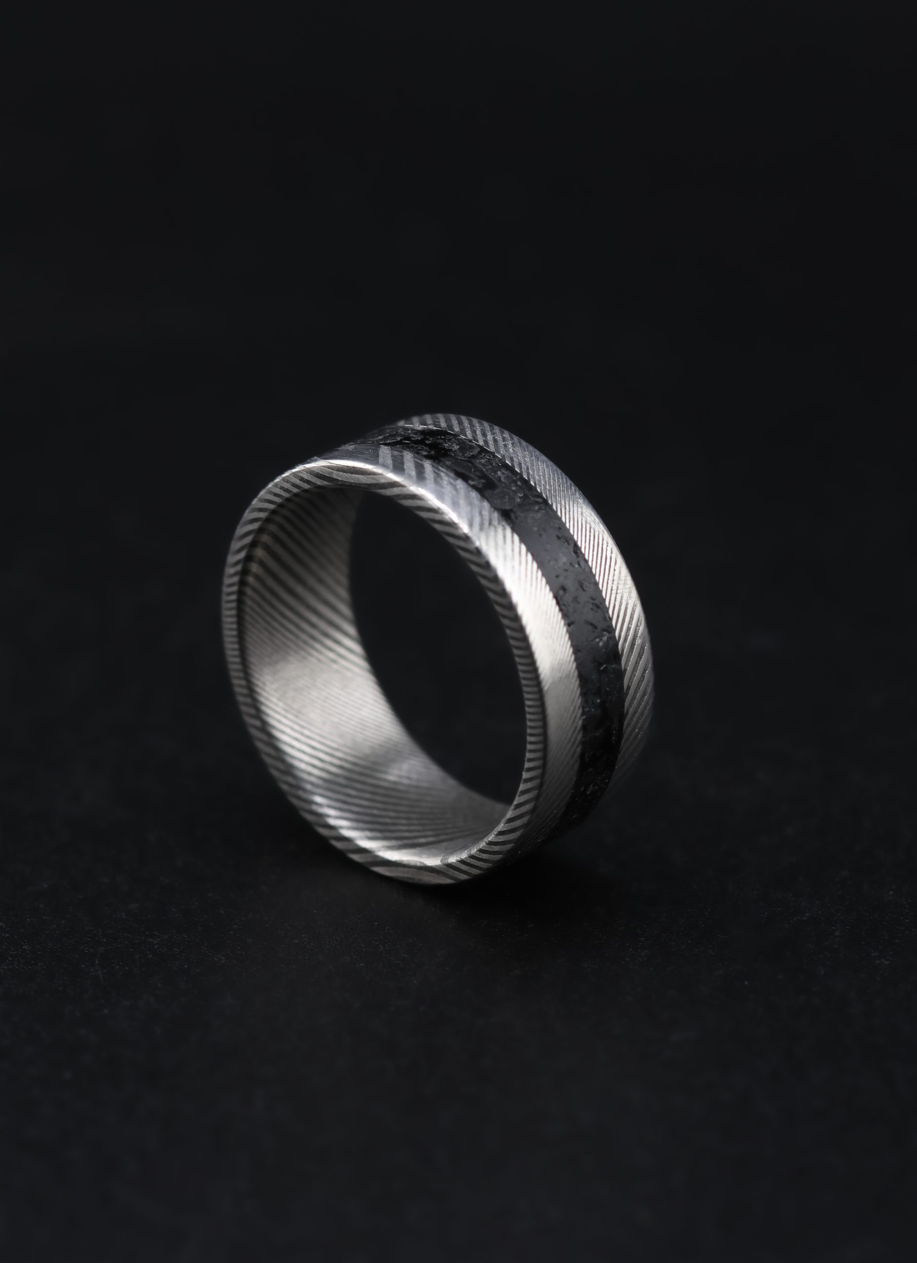 9E2A6539 An 8mm men’s wedding ring made from twisted stainless steel Damascus with a central black obsidian inlay. The ring has a flat profile and a lightweight, durable design. Handmade in Devon by James French.