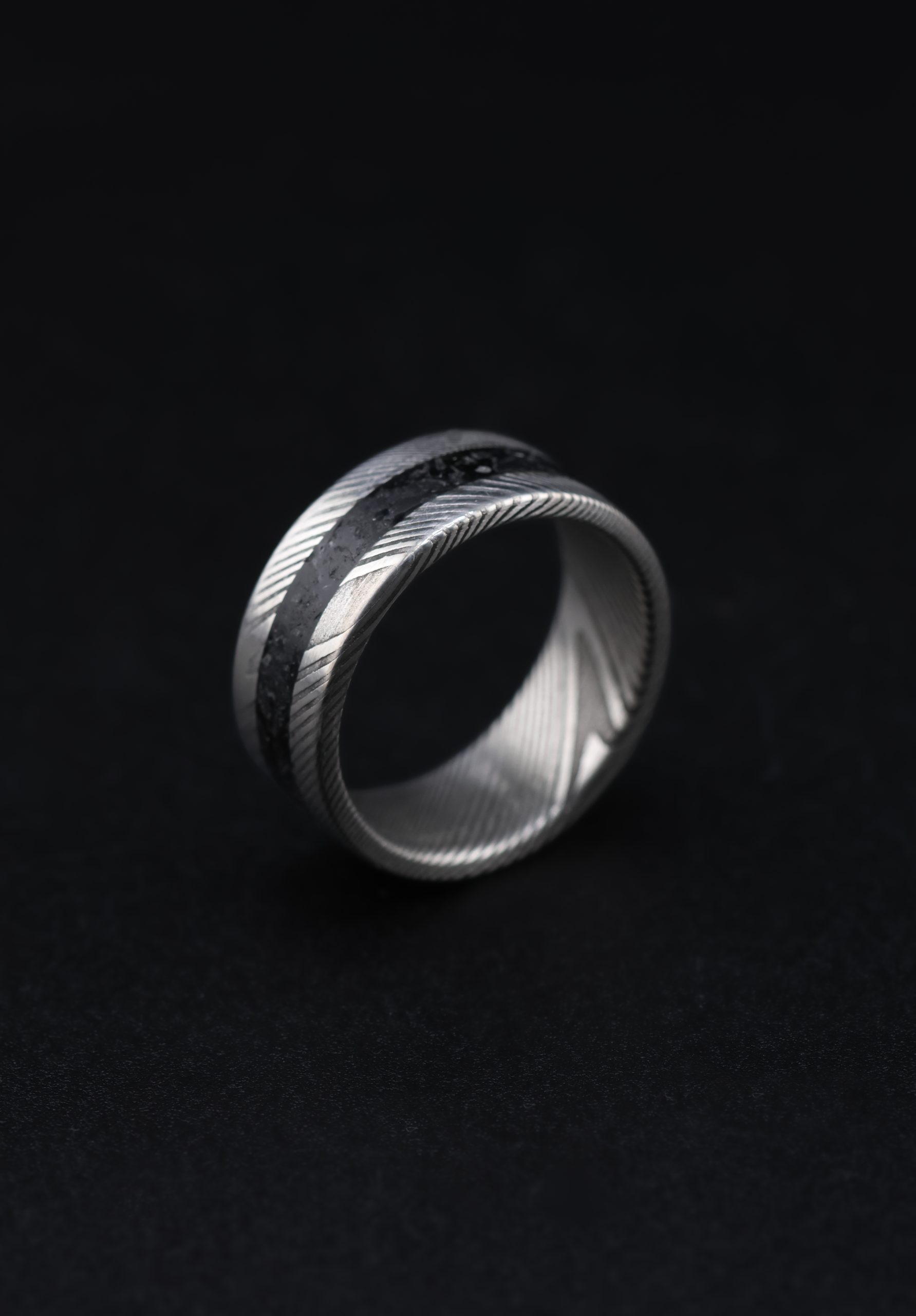 9E2A6541 An 8mm men’s wedding ring made from twisted stainless steel Damascus with a central black obsidian inlay. The ring has a flat profile and a lightweight, durable design. Handmade in Devon by James French.